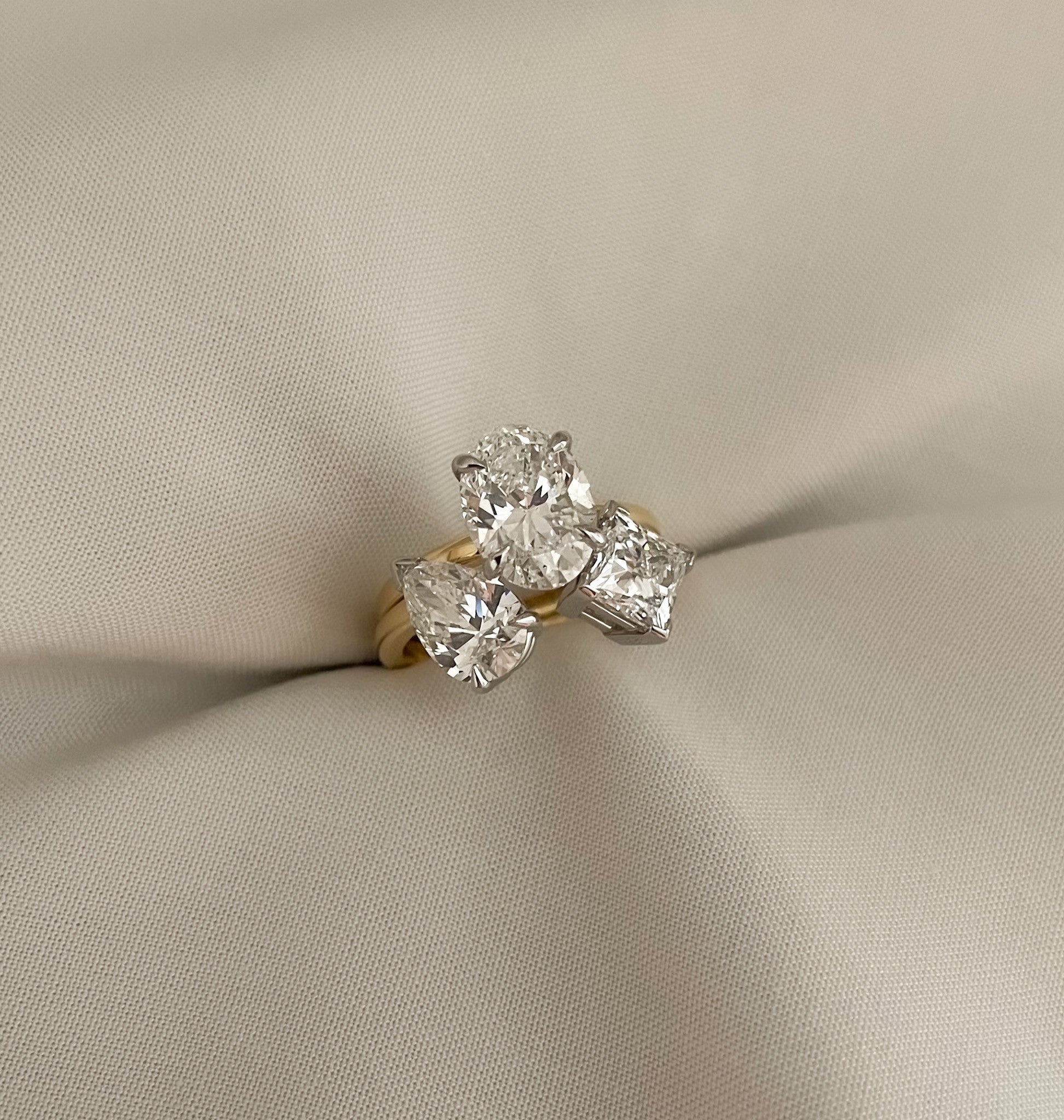 Two stone open ring with pear and princess shape diamonds either side of an oval diamond, on a yellow gold band
